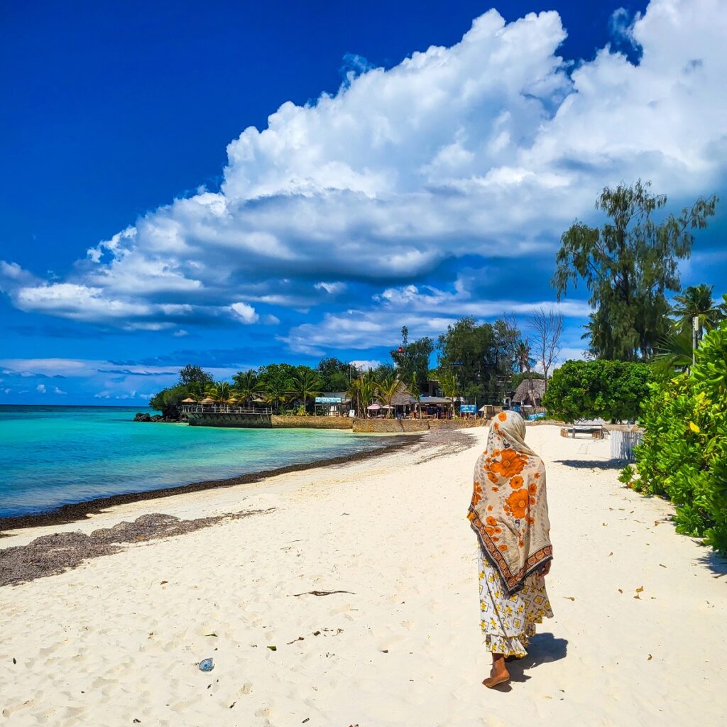 žena v tradičním oděvu se prochází po pláži na Zanzibaru