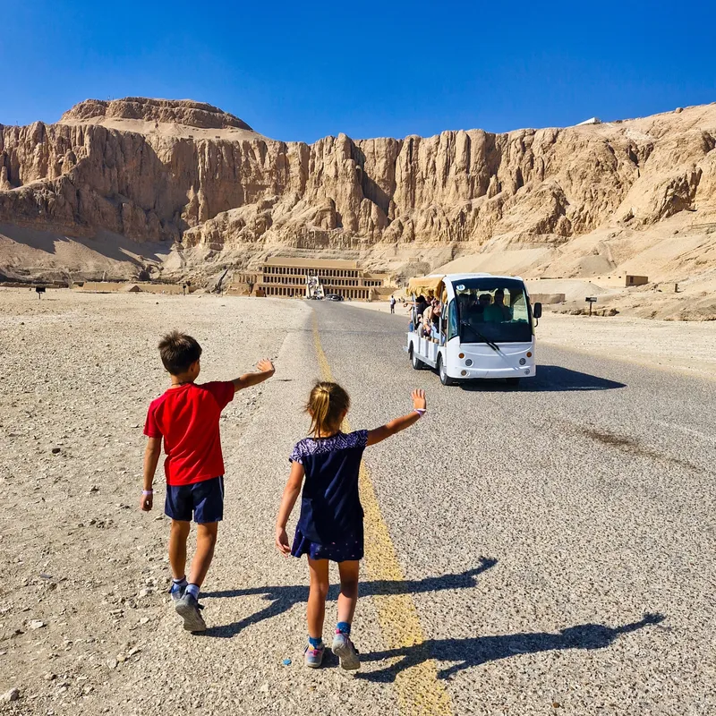 děti mávající na elektrický autobus jedoucí po hlavní silnici od chrámu Hatšepsut v Luxoru v Egyptě