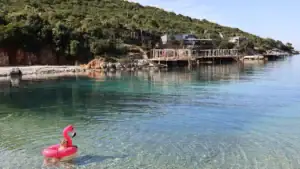 malá holčička plave na růžovém plameňákovi v modré vodě na pláži Augusto The last bay v Ksamilu na albánské riviéře
