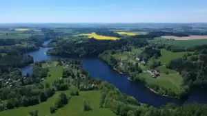 Letecká fotografie zachycuje Pastvinskou přehradu v Orlických horách obklopenou zelenými loukami, lesy a rekreačními oblastmi. Oblíbené místo pro koupání, turistiku a rodinnou dovolenou.