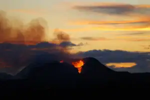 Noční erupce sopky na Islandu, kráter chrlící oranžově žhnoucí lávu