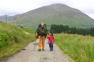 Táta s dcerou jdou po West Highland Way v dešti s velkými batohy