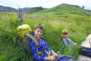Děti s batohy odpočívají během túry na West Highland Way ve Skotsku
